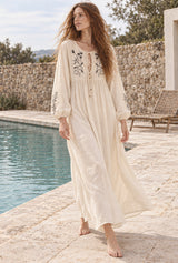 Meadow Stitch cream embroidered maxi dress, walking editorial view with AI-generated adult model