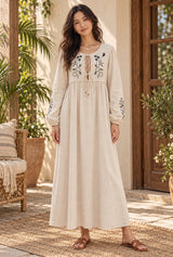 Meadow Stitch beige embroidered maxi dress styled on an AI-generated adult model in a warm bohemian veranda