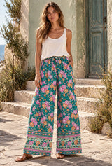 Woman wearing Meadow Green floral wide leg pants in a sunlit bohemian courtyard, full-body editorial view