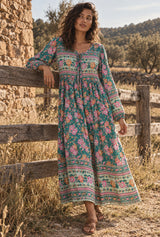 Emerald Wildflower green floral maxi dress on an AI-generated adult model by a rustic timber fence